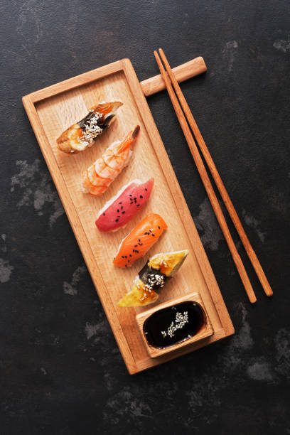 diverse sushi set op een houten plaat, donkere stenen achtergrond. aziatisch eten sushi, sojasaus, eetstokjes. bovenaanzicht, kopieerruimte. - sushischotel stockfoto's en -beelden