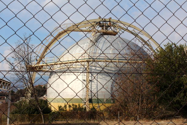 istock Large sphere storage structure with metal steps on one side surrounded with dried grass and trees in front of dense wire fence 1134069398