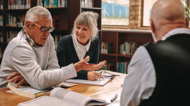 istock Senior classmates having a discussion sitting in a library 1134070088