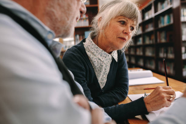 istock Senior couple sitting in library reading books 1134070279