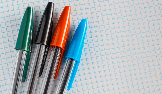 Un grupo de bolígrafos con tapas de colores en una hoja de papel cuadrado de un cuaderno photo