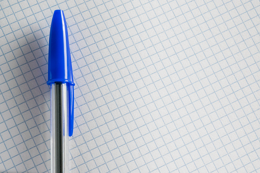 Un bolígrafo con una tapa azul en una hoja de papel cuadrado de un cuaderno photo