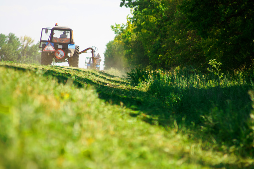 Tractor with a mechanical mower mowing grass on the side of the asphalt road. Road improvement road services. Cleaning of adjacent areas.