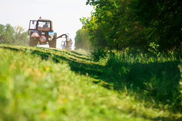 Photo of Tractors machines mowing lawn grass along road