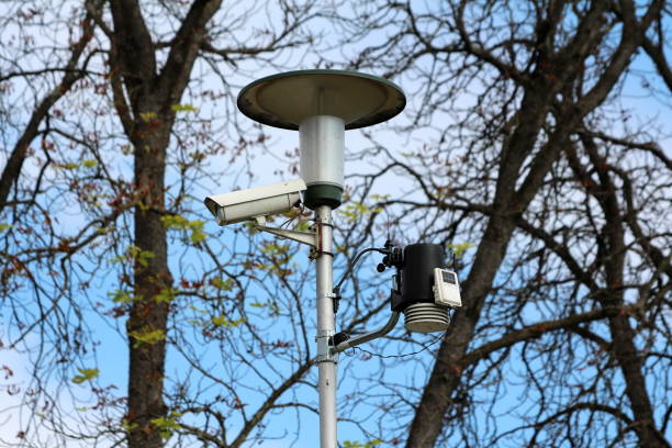 istock Street light on metal post with mounted surveillance camera and various measuring devices with clear blue sky and trees in back 1134078239