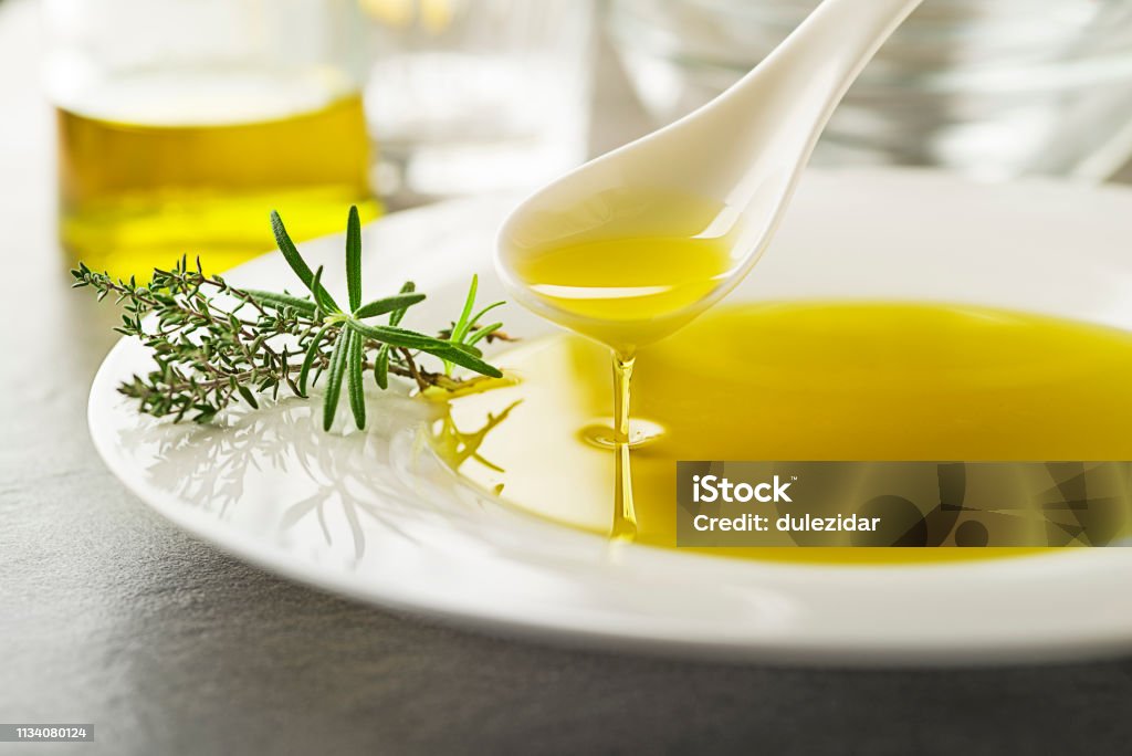Olive oil with herbs Healthy olive oil with herbs pouring with spoon close up Olive Oil Stock Photo
