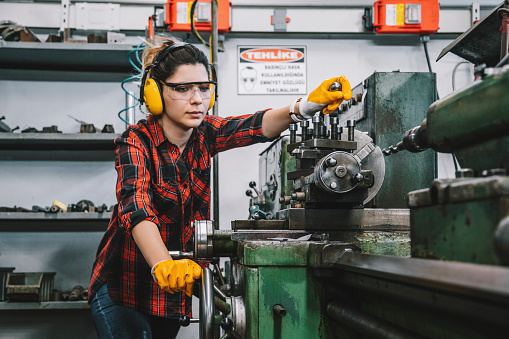 Portrait of hard working female industry technical worker or engineer woman confident serious face turner standing works on automatic universal cnc vertical milling machine for production of metal structures in an industrial manufacturing factory company. XXXL