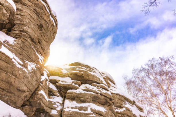 Granite layered rocks covered with snow against the blue sky. The sun looks out from behind the rock.