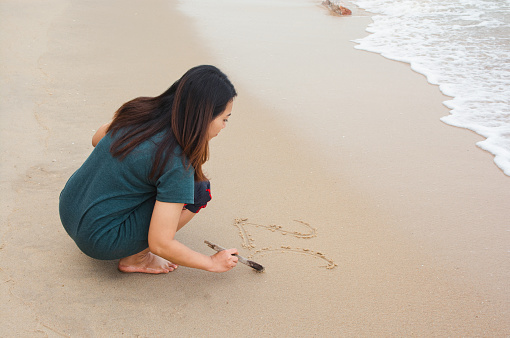Woman writing on sandy beach with tree branch