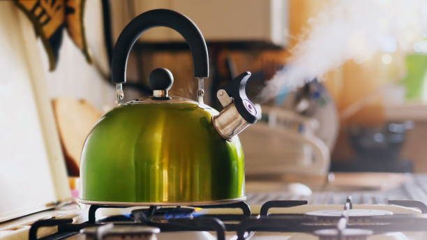 Kettle Boiling On a Gas Stove Kettle boiling on a gas stove. Boiling green kettle boiling with steam emitted from spout. Shallow depth of field. Solar glare from the kitchen window burner stove top stock pictures, royalty-free photos & images