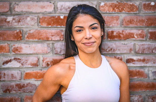 Close-up of smiling woman against brick wall. She is looking at camera. Sporty female is in sportswear. She is beautiful.