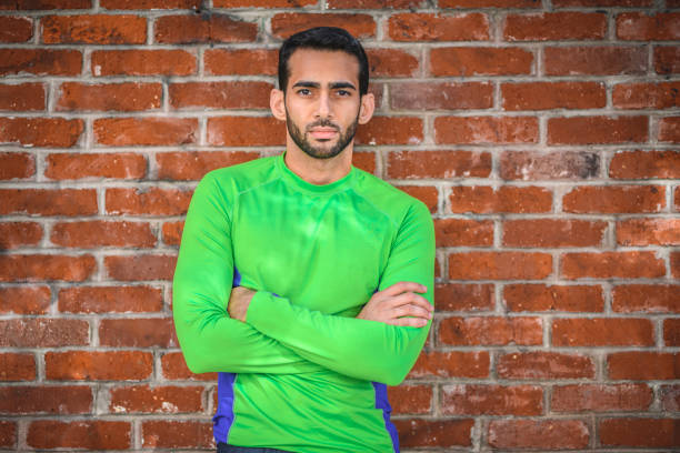 Close-up of thoughtful man against brick wall and looking at camera. Sporty male is in sportswear. He is with arms crossed.