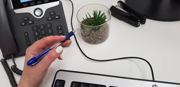 woman holds blue plastic pen in left hand over office phone - child office chaos computer monitor imagens e fotografias de stock