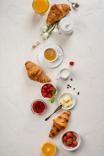 Continental breakfast captured from above top view, flat lay . Coffee, orange juice, croissants, jam, berry, milk and flowers. Grey stone worktop as background. Layout with free text copy space.