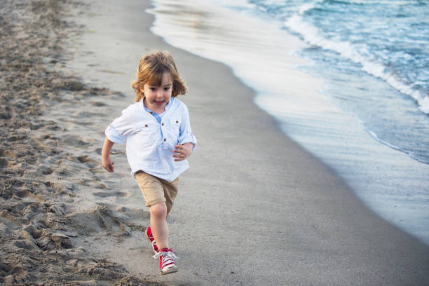 Little child running on the beach Little blonde child running on the beach in a gloomy day. trans boy stock pictures, royalty-free photos & images