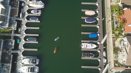 Aerial shot of a family on two standup paddleboards paddling through a marina with motorboats, sailboats, and houses.