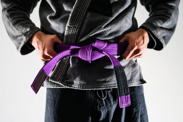 close up on brazilian jiu jitsu bjj fighter in a gi kimono holding purple belt around his taille - ju jitsu stock-fotos und bilder