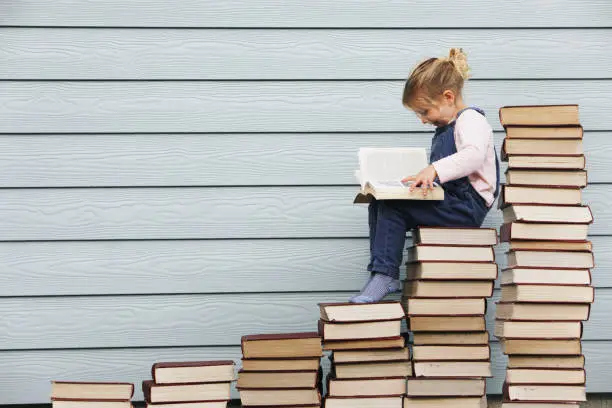 Photo of Young girl sits on stack of books