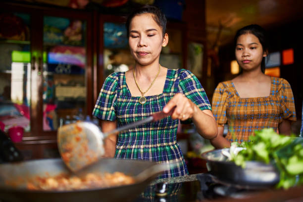 แม่และลูกสาวชาวไทยทําอาหารด้วยกันในห้องครัวแบบชนบททําแกงแดง