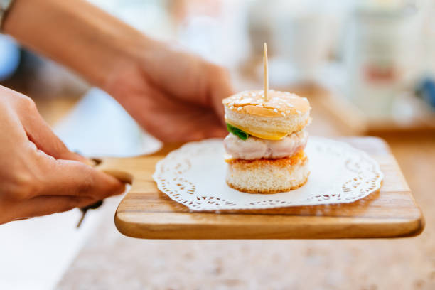 Female hand serving Mini Chicken Burger on wooden chopping board with blur background.