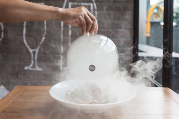 la mano maschile solleva la cloche di vetro da un piatto con cibo caldo e fumo in movimento al ristorante - ora di cibo affumicato! da vicino. - tenda igloo foto e immagini stock