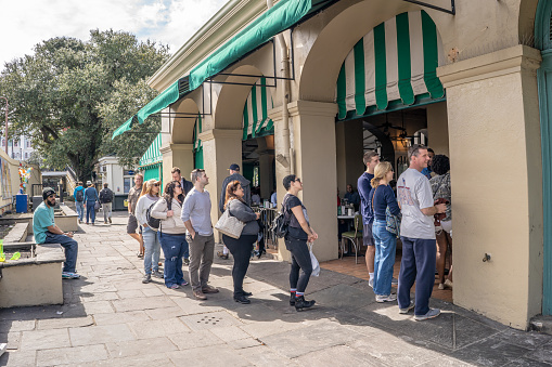 New Orleans, Louisiana / USA - February 14, 2019: People wait in line at the to-go counter at the famous Cafe Du Monde restaurant, for beignets, in the French Quarter.
