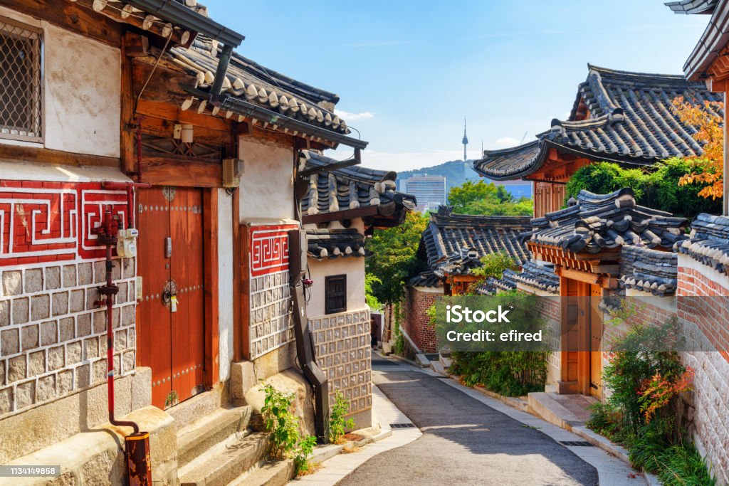 Awesome view of old narrow street and traditional Korean houses Awesome view of cozy old narrow street and traditional Korean houses of Bukchon Hanok Village in Seoul, South Korea. Seoul Tower on Namsan Mountain is visible on blue sky background. Scenic cityscape. Seoul Stock Photo