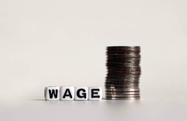 istock 'WAGE' text in white cube and a pile of coins. 1134159875