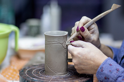 Hands of artist who make a mug from ceramic clay in studio