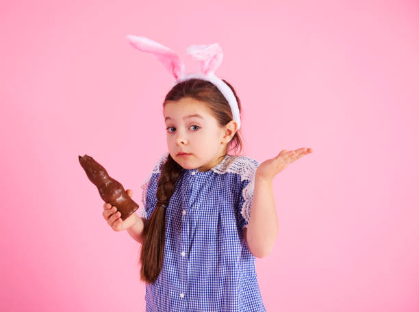 chica confundida comiendo conejo de chocolate en el estudio - easter easter bunny fun humor fotografías e imágenes de stock