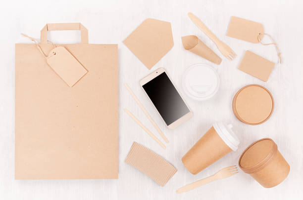 istock Blank different cardboard packaging for fast food - bag, coffee cup, screen phone, cutlery, sugar, spice, container and box for soup on white wood board. 1134178332