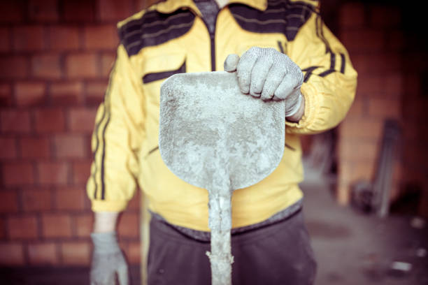 Photo of Skilled Mid Aged Manual Worker At Construction Site. He is Wearing Blue Protective Helmet and Holding a Shovel.