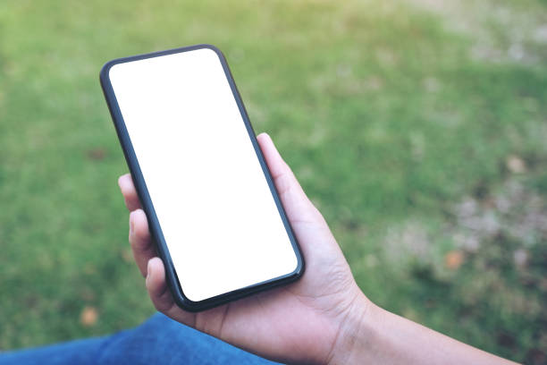 istock Mockup image of a woman holding and using black smart phone with blank white desktop screen in outdoor with green nature background 1134183278