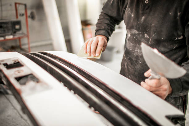 istock Car repair technician using a wide scraper and a sand paper to work on a bumper that got damaged in an accident 1134186881