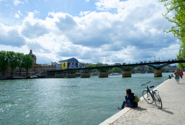Paris, France - April 25, 2018: Young woman resting with a bicycle on the quay along the Seine River in Paris