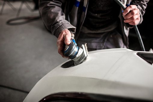 Using a portable small buffer to buff out excess paint on a car bumper that got damaged in a car accident.