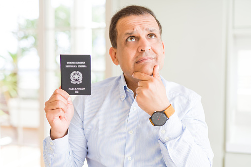 Middle age man holding holding passport of Italy serious face thinking about question, very confused idea