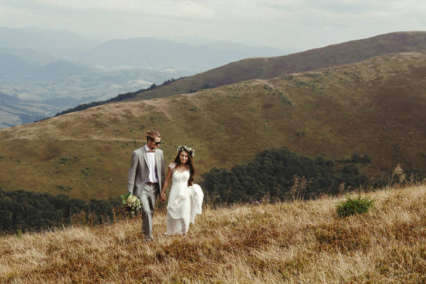 istock happy gorgeous bride and groom walking  in sun light holding hands, boho wedding couple, luxury ceremony at mountains with amazing view, space for text 1134190828