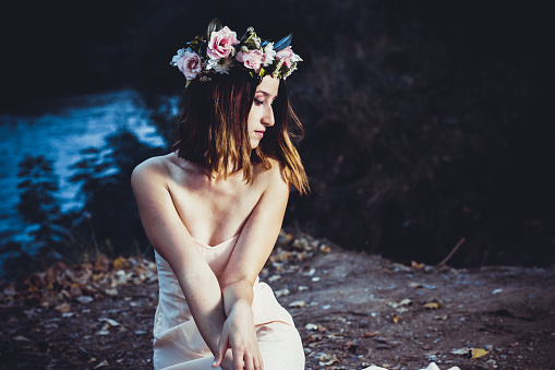 Young brunette beauty with floral wreath on her head in nature at dusk.