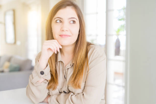 istock Beautiful young woman at home with hand on chin thinking about question, pensive expression. Smiling with thoughtful face. Doubt concept. 1134217824