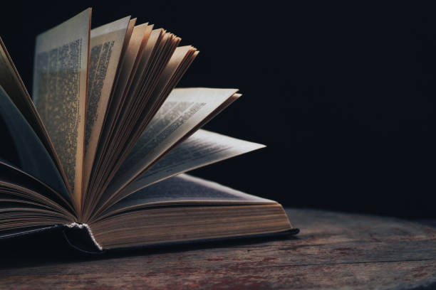 istock One open old book on a round wooden table. Beautiful dark background.. 1134221018