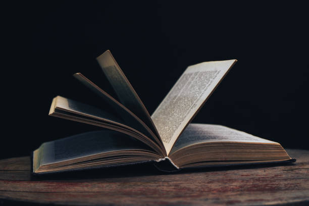 istock One open old book on a round wooden table. Beautiful dark background.. 1134221085