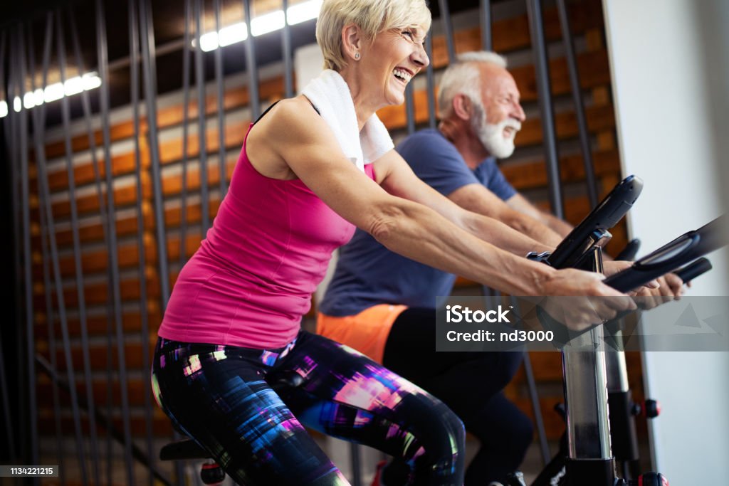 Mature fit people biking in the gym, exercising legs doing cardio workout cycling bikes Fit senior people biking in the gym, exercising legs doing cardio workout cycling bikes Senior Adult Stock Photo