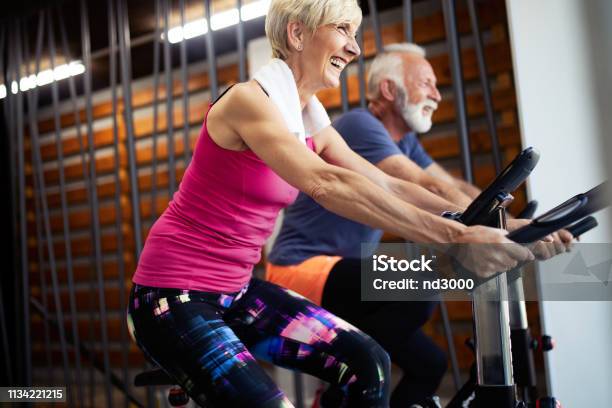 Mature Fit People Biking In The Gym Exercising Legs Doing Cardio Workout Cycling Bikes Stock Photo - Download Image Now