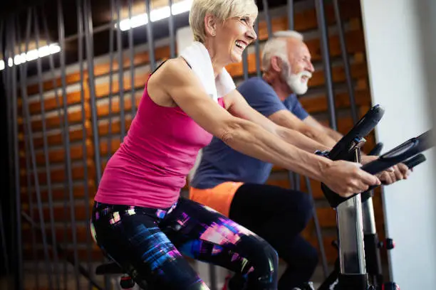 Fit senior people biking in the gym, exercising legs doing cardio workout cycling bikes