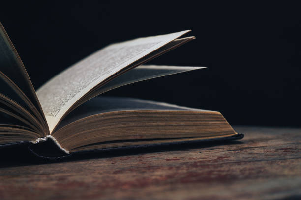 istock One open old book on a round wooden table. Beautiful dark background.. 1134221578