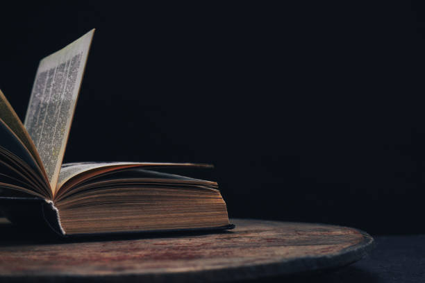 istock One open old book on a round wooden table. Beautiful dark background.. 1134221668