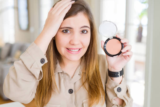 istock Beautiful young woman using make up cosmetics applying powder stressed with hand on head, shocked with shame and surprise face, angry and frustrated. Fear and upset for mistake. 1134222359