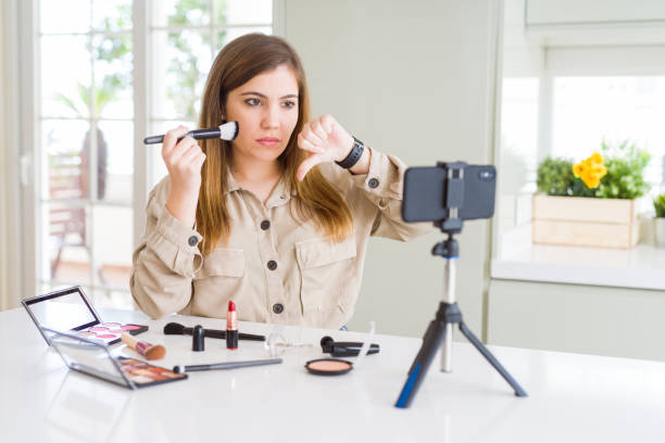 istock Beautiful young influencer woman recording make up video tutorial with angry face, negative sign showing dislike with thumbs down, rejection concept 1134223283