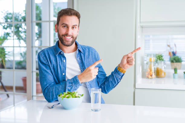 istock Handsome man eating fresh healthy salad smiling and looking at the camera pointing with two hands and fingers to the side. 1134228570